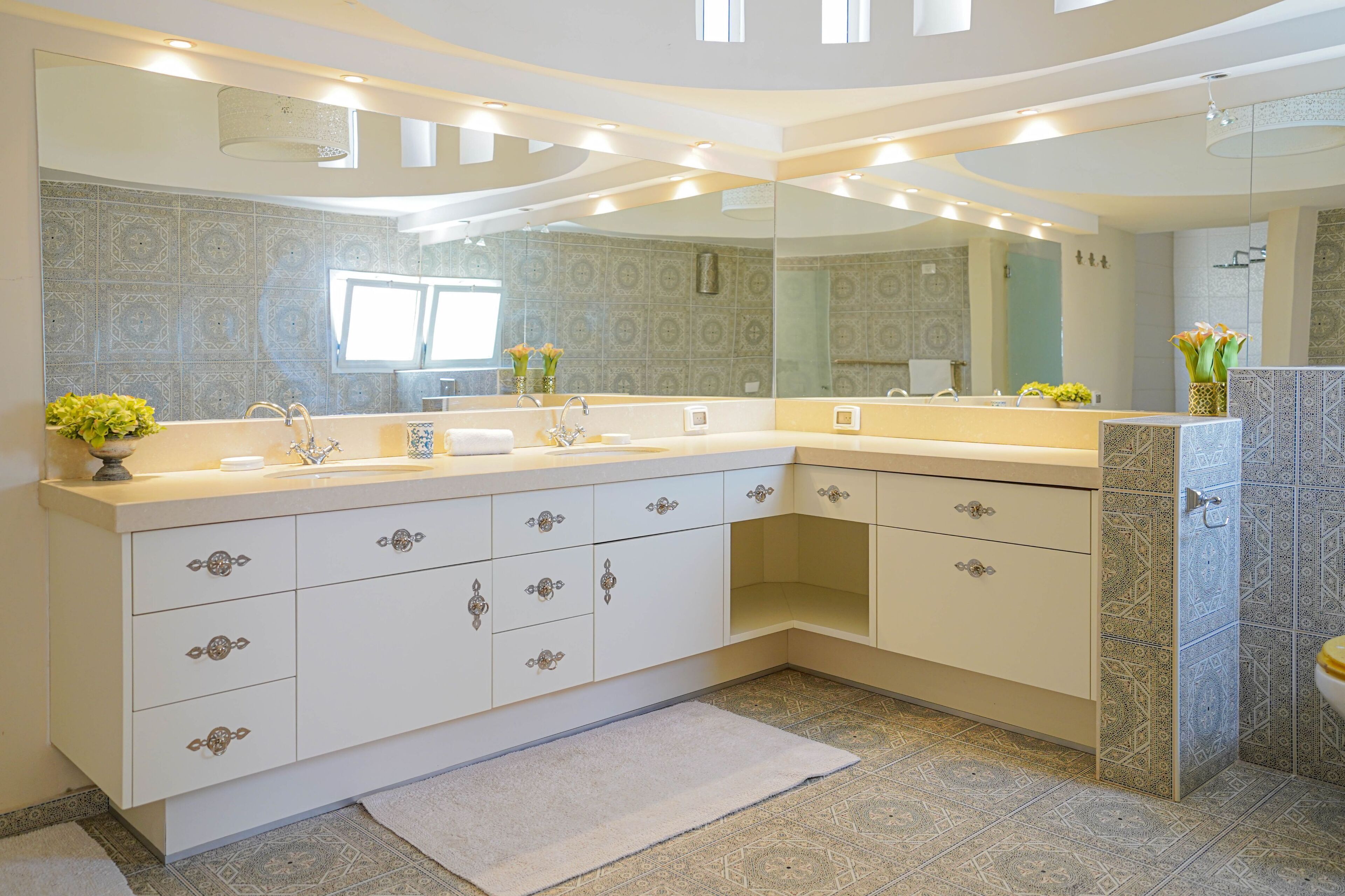 A modern bathroom with a large vanity, multiple drawers, a mirror, and patterned tiles.