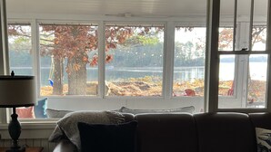 A living room with a sofa, a lamp, and a view of a lake and autumn trees. - Historic but HiTech, modern Burleigh Falls cottage on Stony Lake. Amazing views (Harcourt)