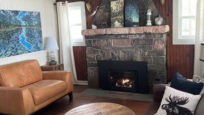 A cozy living room with a stone fireplace, leather sofas, a round coffee table, and a ceiling fan. - Historic but HiTech, modern Burleigh Falls cottage on Stony Lake. Amazing views (Harcourt)