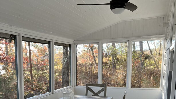 A covered patio with a wooden table and chairs, large windows, and a ceiling fan. - Historic but HiTech, modern Burleigh Falls cottage on Stony Lake. Amazing views (Harcourt)