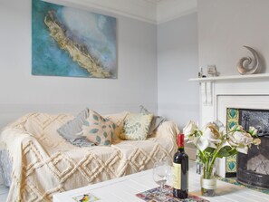 Un salón acogedor con un sofá, una chimenea, una mesa con una botella de vino y copas, y un cuadro en la pared.
