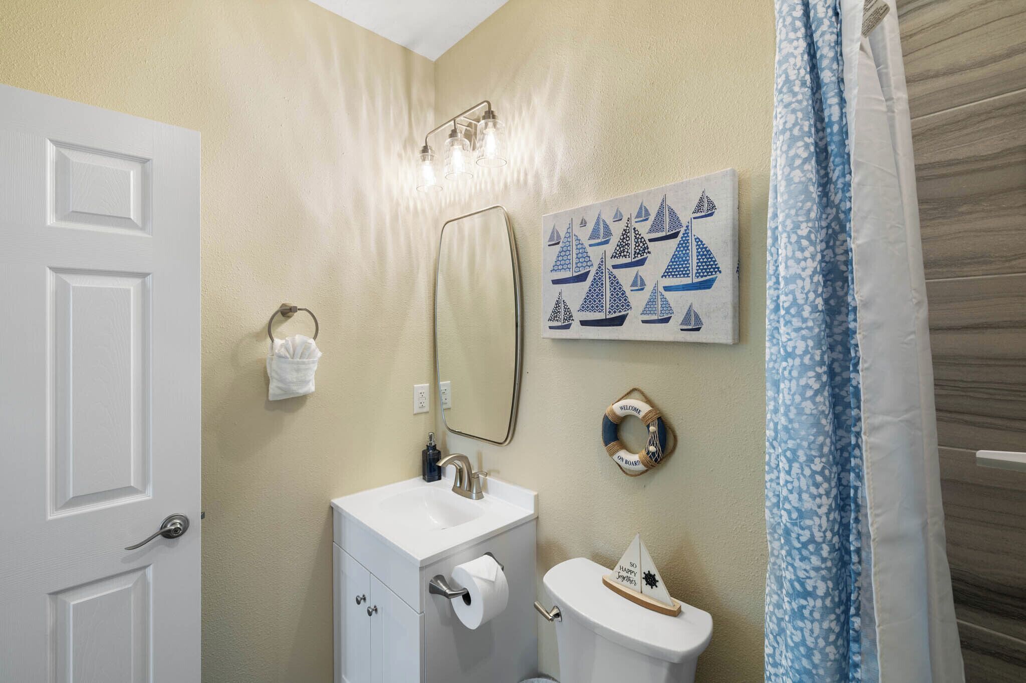 A bathroom with a white sink, toilet, and a towel rack. There is a mirror above the sink and a wall-mounted light fixture.