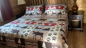 A wooden-paneled room with a bed featuring a patterned quilt and two bedside lamps. - Northern Flare cabin with mountain view 5 min from Nordic Eclipse (Whitehorse)
