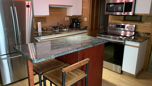 A modern kitchen with stainless steel appliances, a granite countertop, wooden bar stools, and a wooden ceiling. - Northern Flare cabin with mountain view 5 min from Nordic Eclipse (Whitehorse)