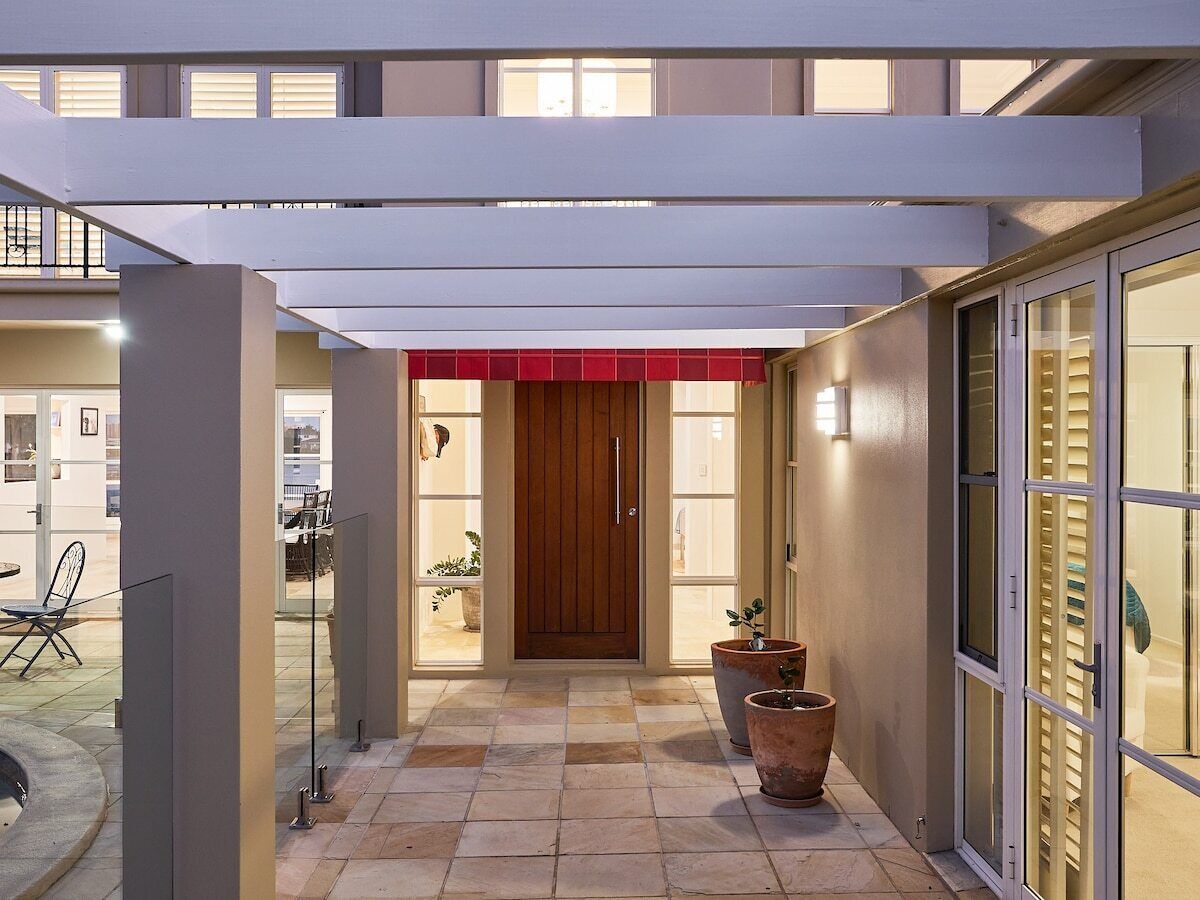 A covered outdoor area with a wooden door, potted plants, and a glass door leading to a balcony.