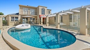 Ein Schwimmbad mit Whirlpool, eine überdachte Terrasse und ein zweistöckiges Haus mit großen Fenstern und einem Balkon.