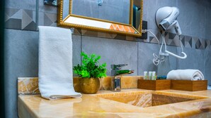 Une salle de bain avec un lavabo en marbre, une serviette, une plante en pot, un miroir et un sèche-cheveux.