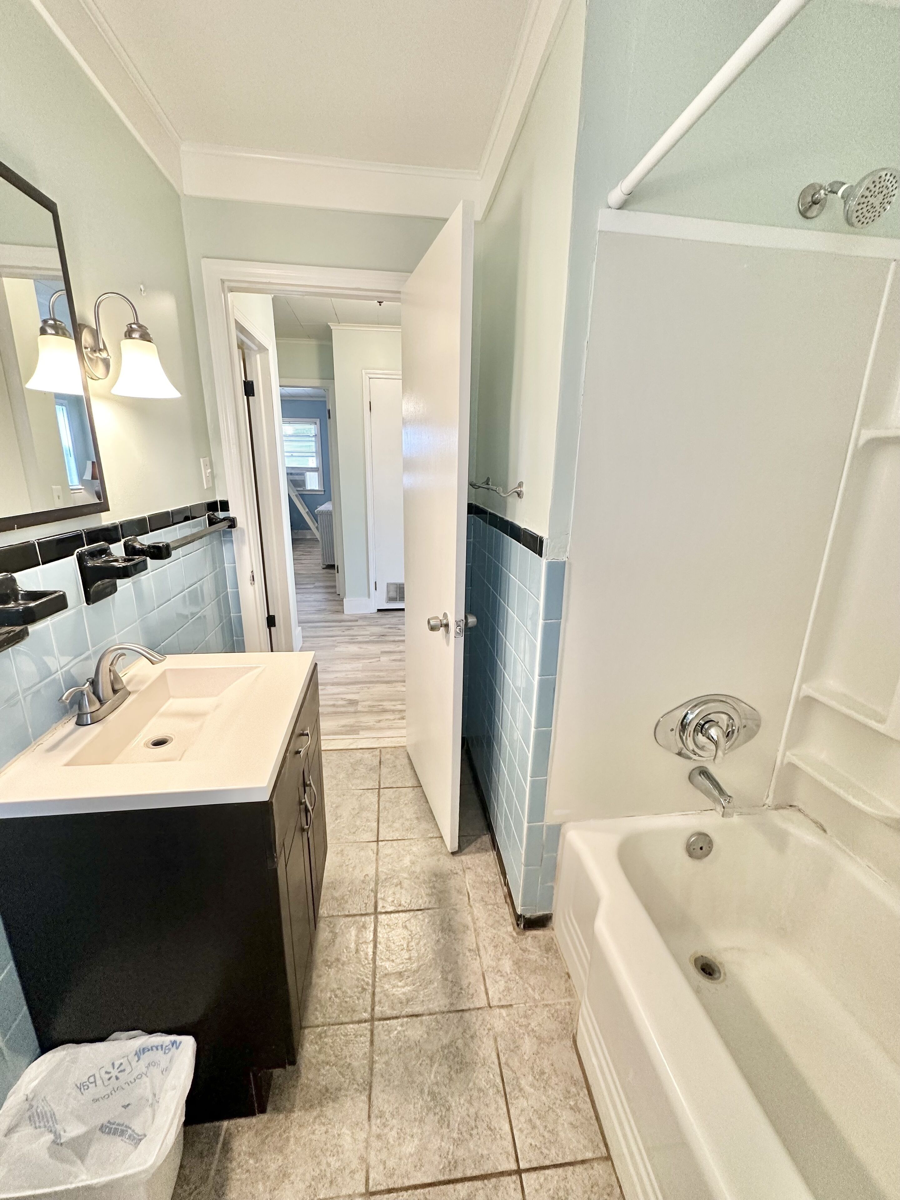 A bathroom with a white bathtub, a sink with a black vanity, and a mirror with two lights.