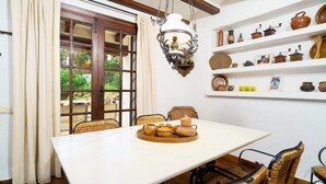 A dining area with a table set for four, surrounded by wicker chairs. A shelf with various pottery items is visible on the wall. - Chalet in El Portet (Moraira)