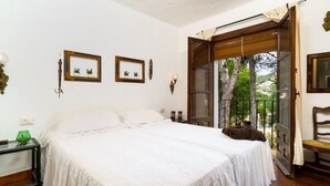 A bedroom with a bed, a nightstand, a window with a view of trees, and a door leading to an outdoor area. - Chalet in El Portet (Moraira)