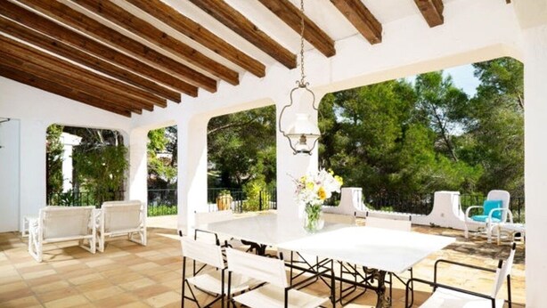 An outdoor patio with a white table and chairs, surrounded by white walls and wooden beams. - Chalet in El Portet (Moraira)