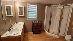 A bathroom with two sinks, a vanity, a mirror, a window with blinds, and a glass shower enclosure. - Riverfront Romantic Getaway (Andrews)