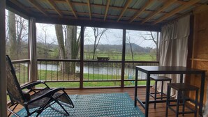 A covered outdoor area with a view of a river, a bench, and a table. - Riverfront Romantic Getaway (Andrews)