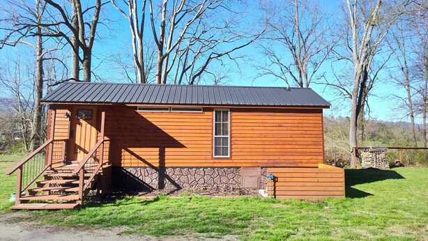 A small wooden cabin with a metal roof, a staircase leading to the entrance, and a stone foundation. - Riverfront Romantic Getaway (Andrews)