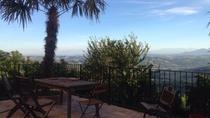 An outdoor patio with a wooden table and chairs, a palm tree, and a view of distant mountains and a valley.