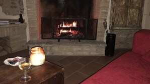 A fireplace with a fire, a glass of wine, and a candle on a table.