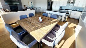 A modern kitchen with white cabinets, a large island, and a dining area with a wooden table and blue chairs. - Best View on Fairway, With ready Hot Tub! (Park City)