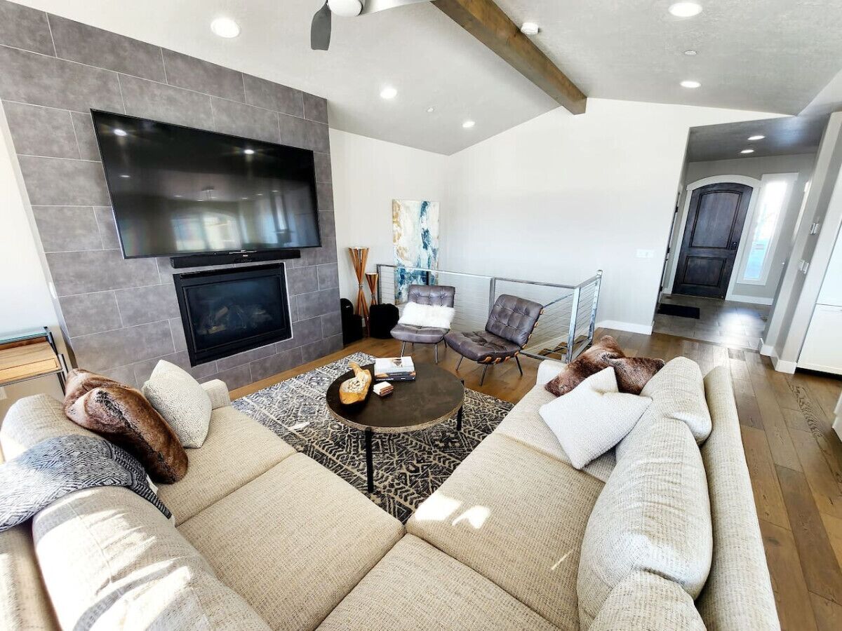 A modern living room with a large sectional sofa, a flat-screen TV mounted on the wall, a fireplace, and a dining area with a glass table.