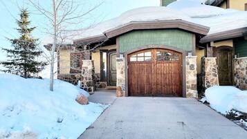 A snow-covered house with a stone facade, a wooden front door, and a chimney.
