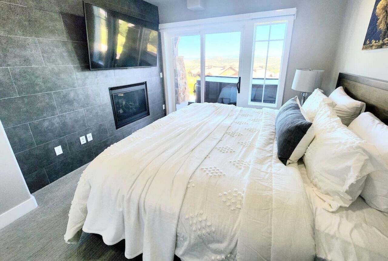 A bedroom with a large bed, a flat-screen TV mounted on the wall, and a sliding glass door leading to an outdoor area.