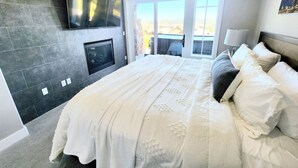 A bedroom with a large bed, a flat-screen TV mounted on the wall, and a sliding glass door leading to an outdoor area. - Best View on Fairway, With ready Hot Tub! (Park City)
