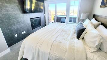 A bedroom with a large bed, a flat-screen TV mounted on the wall, and a sliding glass door leading to an outdoor area.