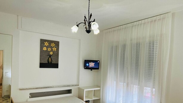 A bedroom with a bed, a TV, a painting, and a window with curtains. - Le Maschere  (Mestre)