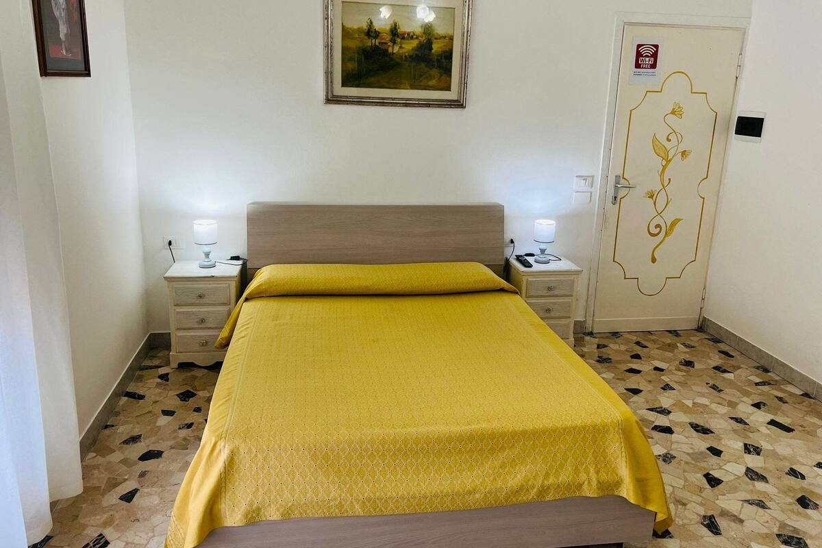 A room with a bed, two bedside tables with lamps, a framed painting on the wall, and a door with a floral design.
