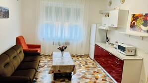 A compact living space with a sofa, a coffee table with flowers, a kitchen area with a microwave, and a refrigerator. - Le Maschere  (Mestre)