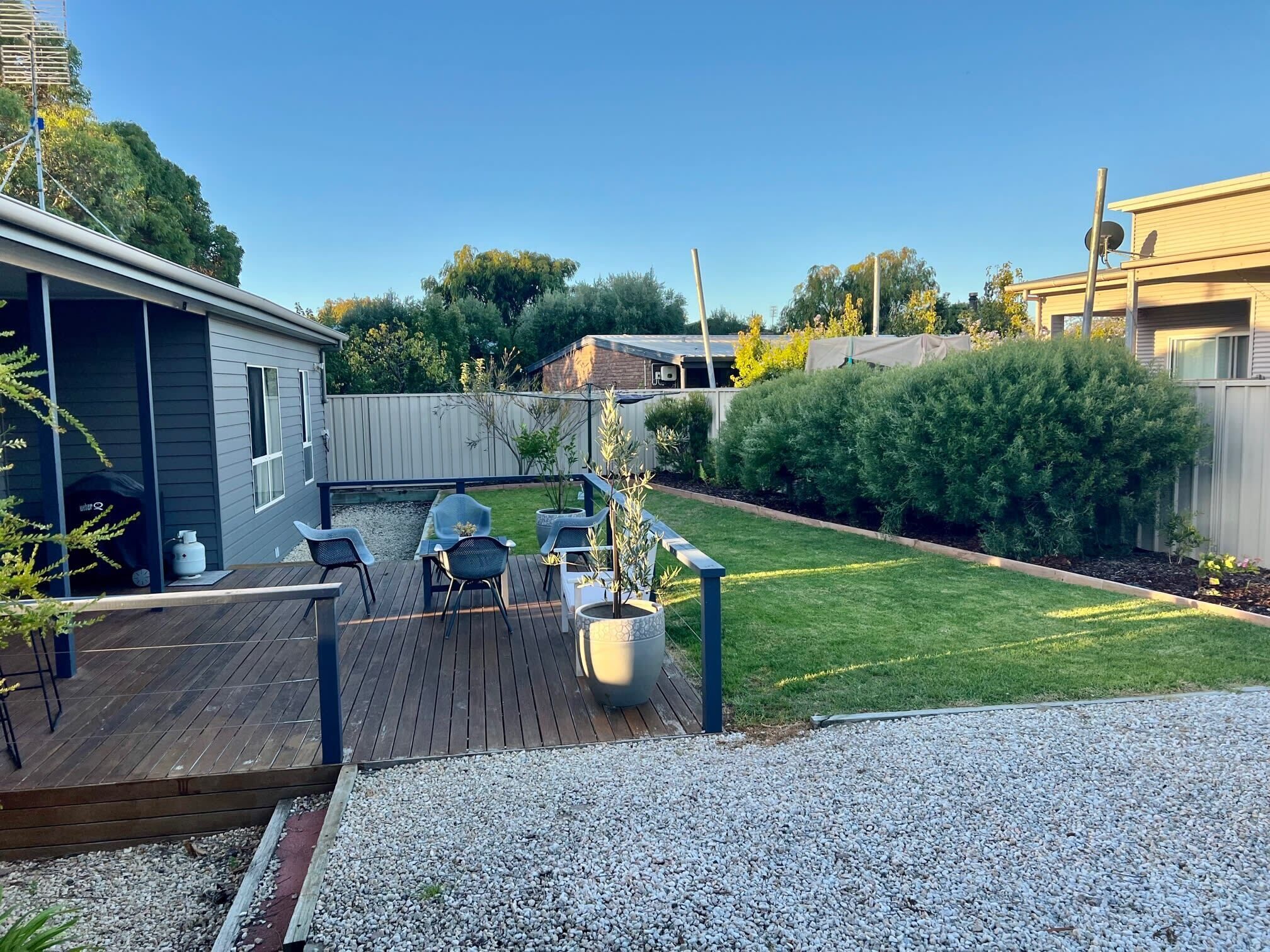 A backyard with a wooden deck, outdoor seating, a lawn, and a fenced area.