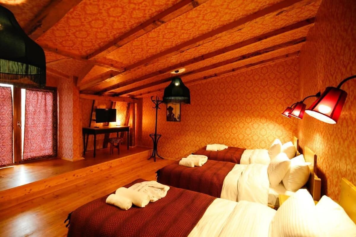 Quarto com duas camas, piso de madeira, papel de parede estampado e uma escrivaninha com cadeira.