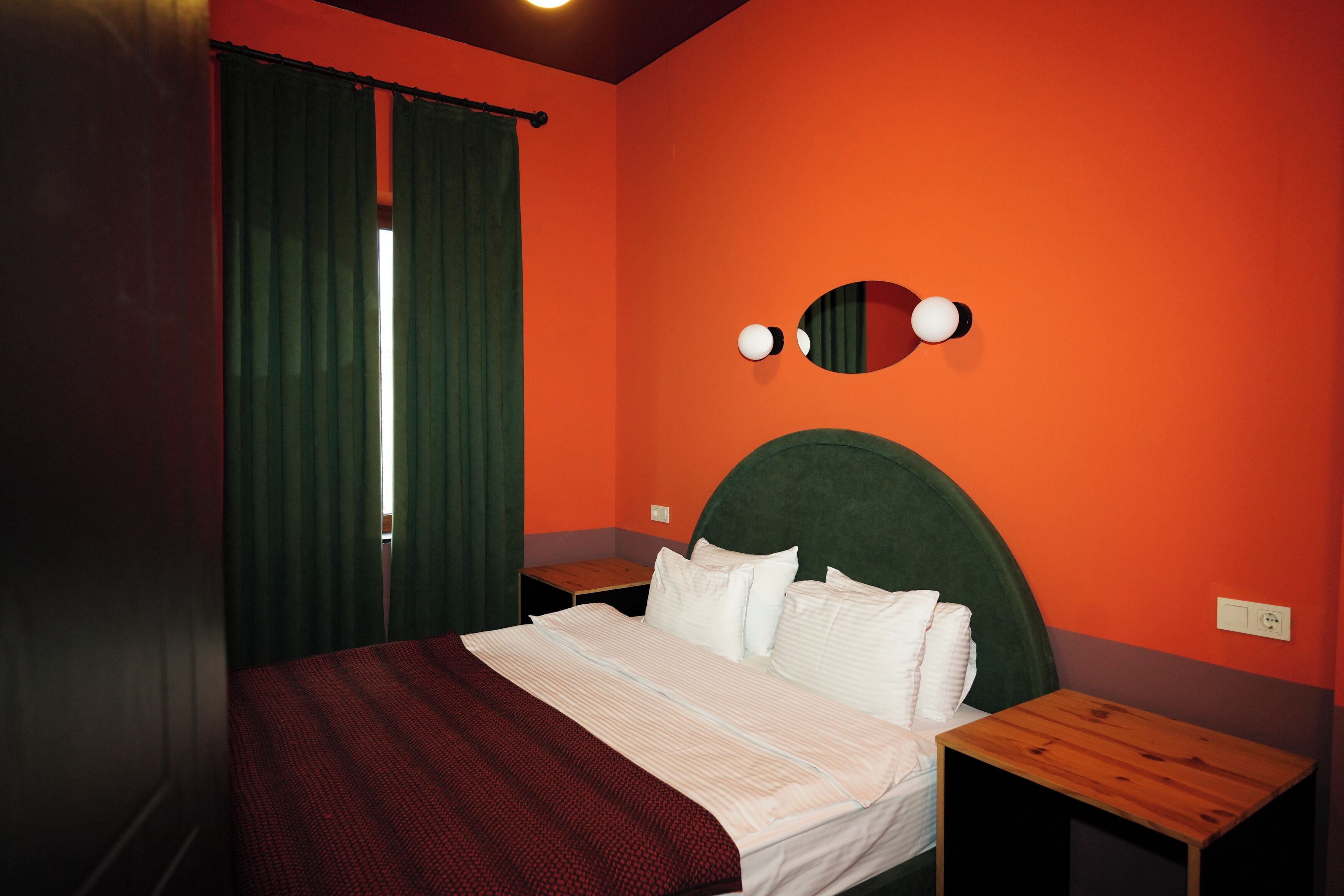 Een slaapkamer met een bed, nachtkastje, spiegel en een raam met gordijnen.