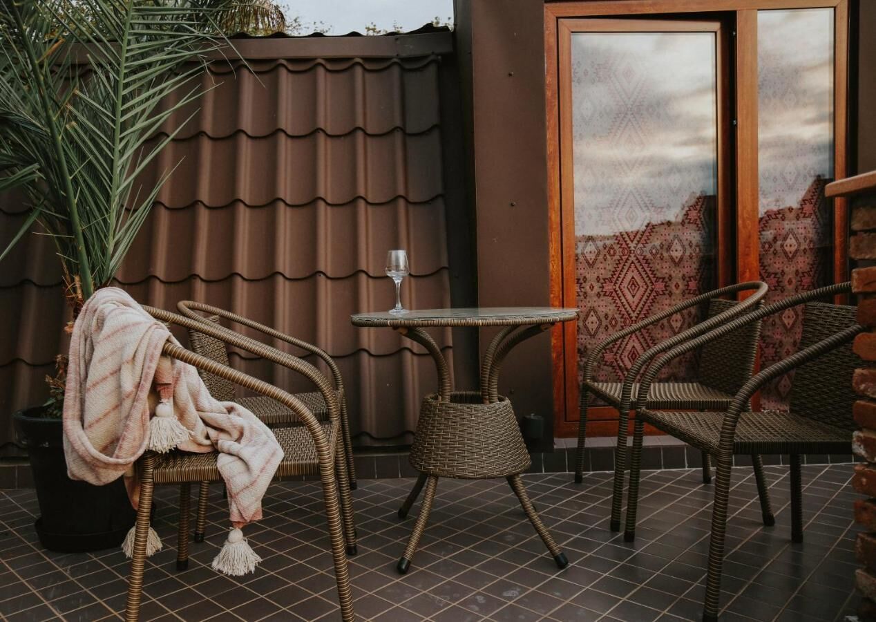A wicker chair with a blanket, a small table with a glass, and a potted plant.
