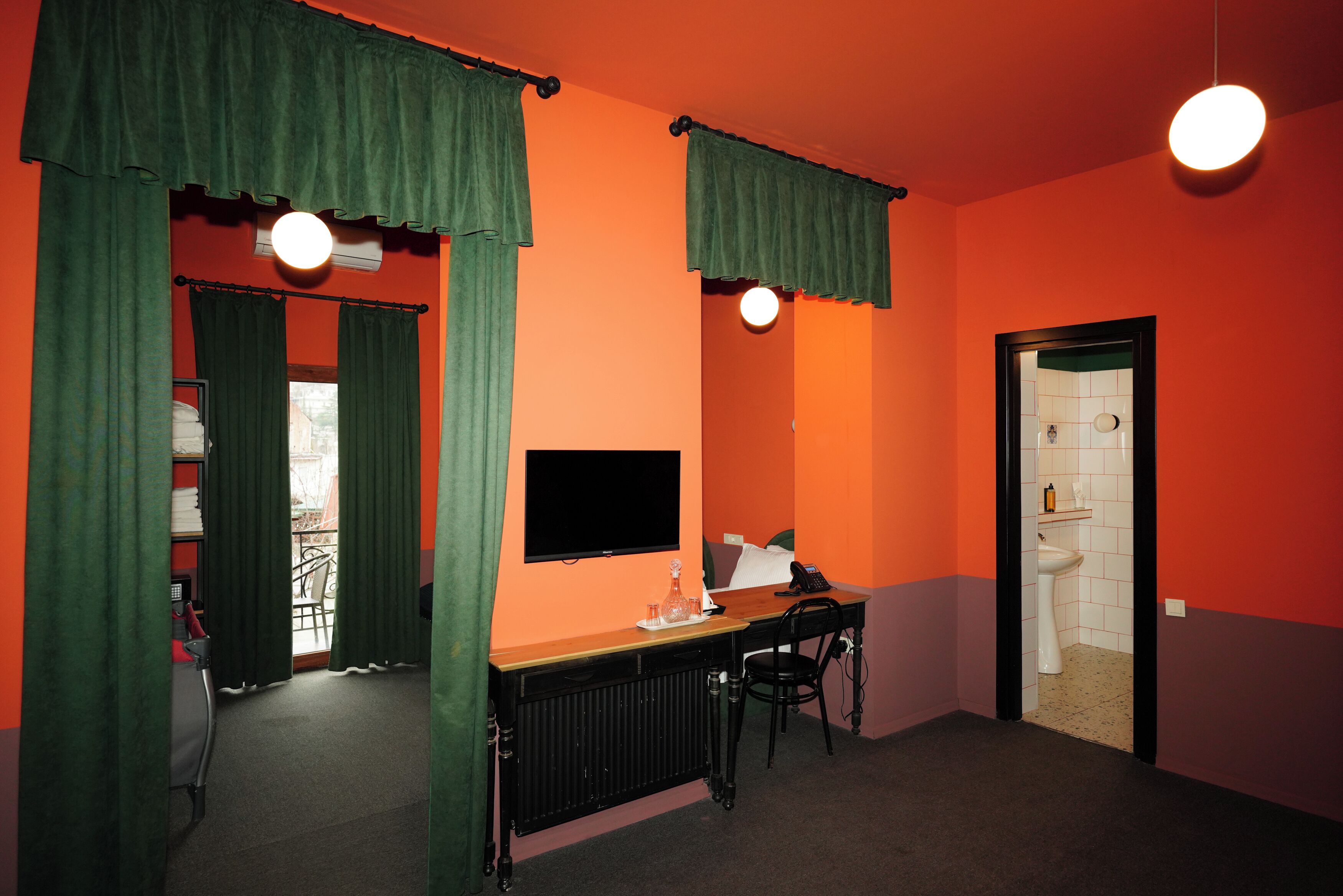 A room with orange walls, a black desk, a chair, a television, and a radiator.