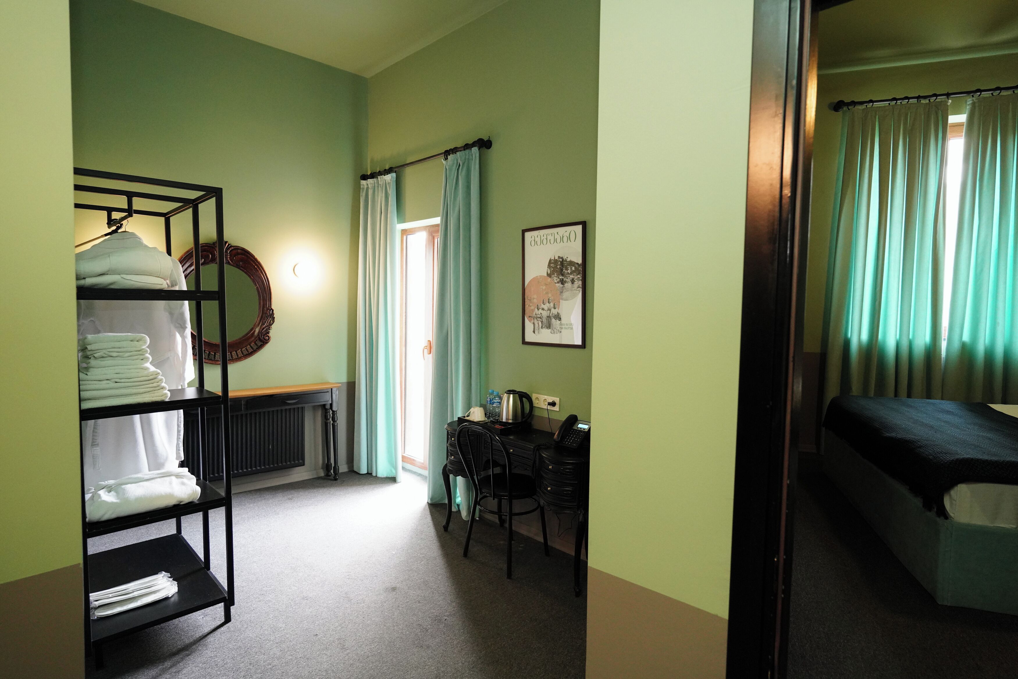 A hotel room with a bunk bed, a desk with a chair, a radiator, and a wall-mounted shelf with folded towels.