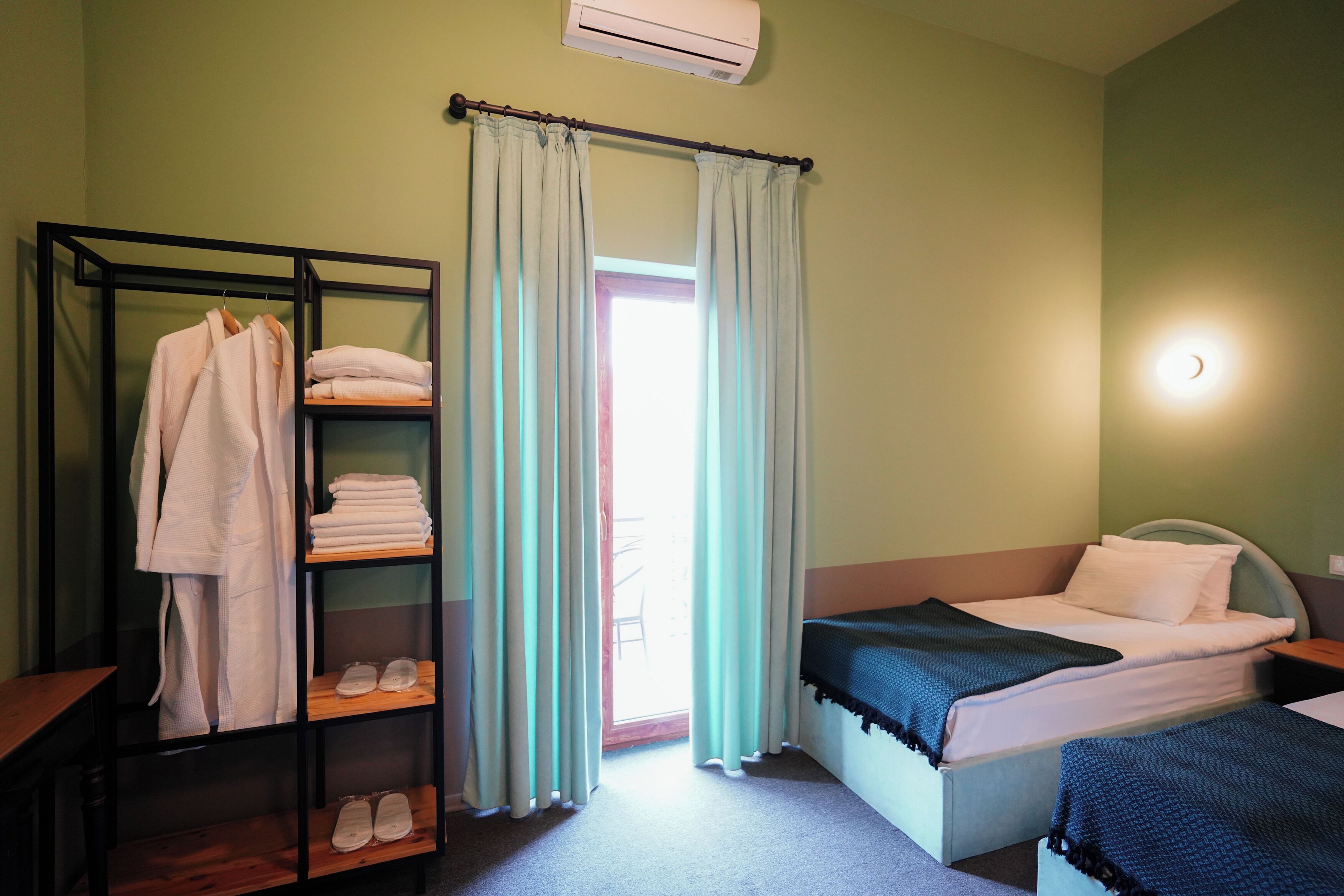 Quarto com uma cama, um armário com toalhas dobradas e um cabideiro com roupas.