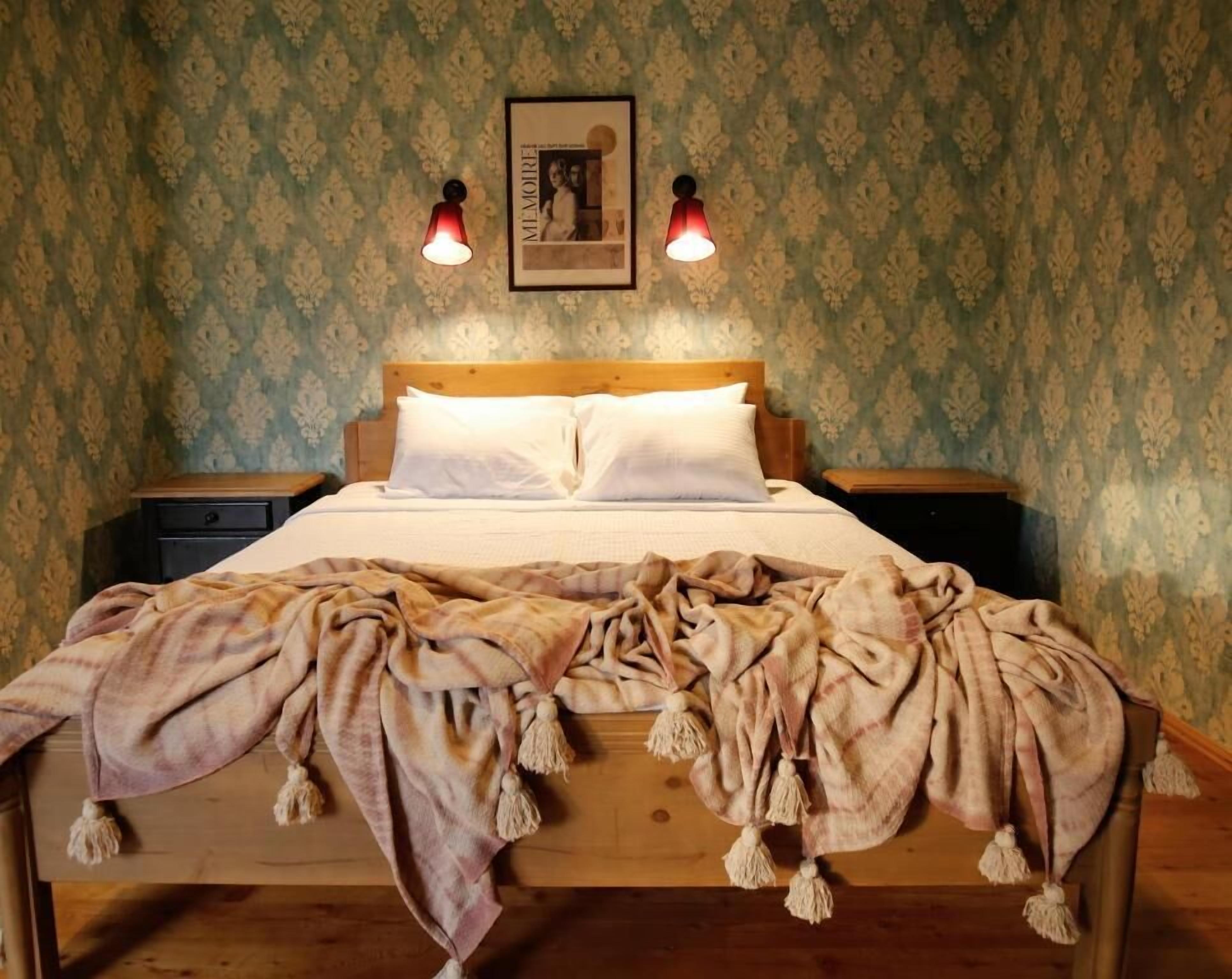 A bedroom with a wooden bed, two bedside tables, a wall-mounted picture, and two wall-mounted lamps.