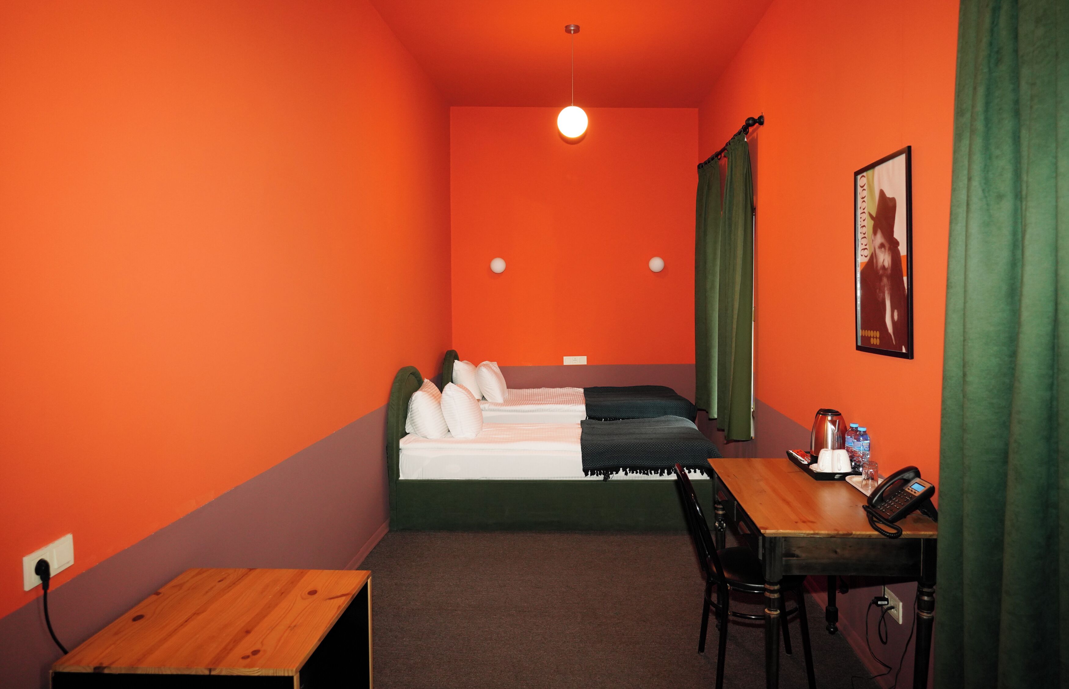 A small room with a single bed, a wooden table, a chair, a desk, and a telephone.