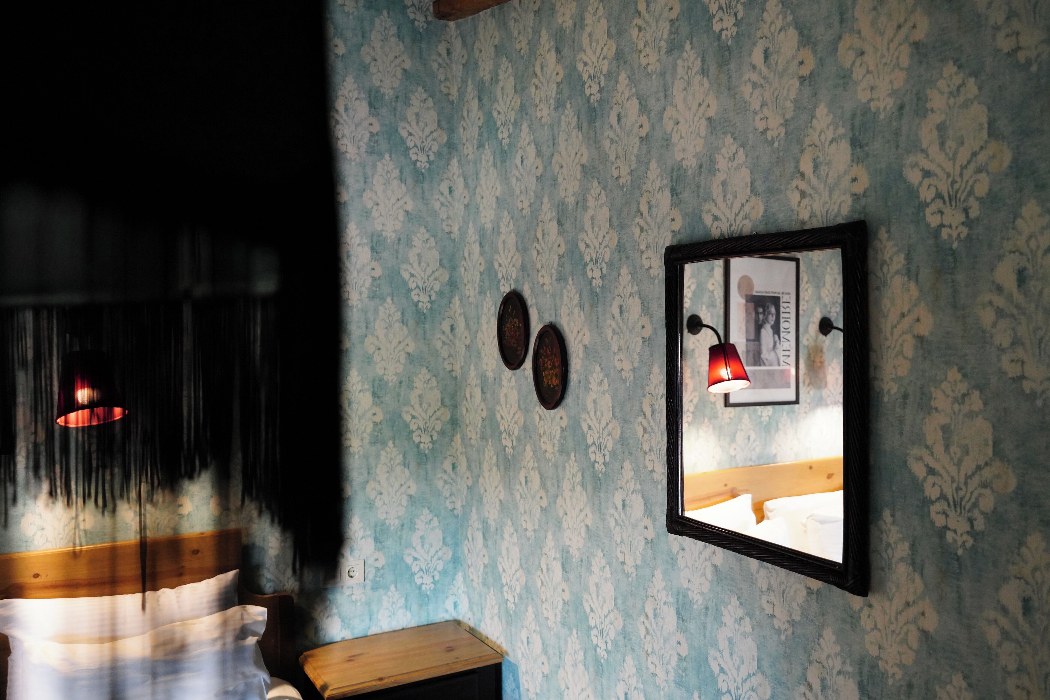 A room with a patterned wallpaper, a framed picture on the wall, and a wooden nightstand.