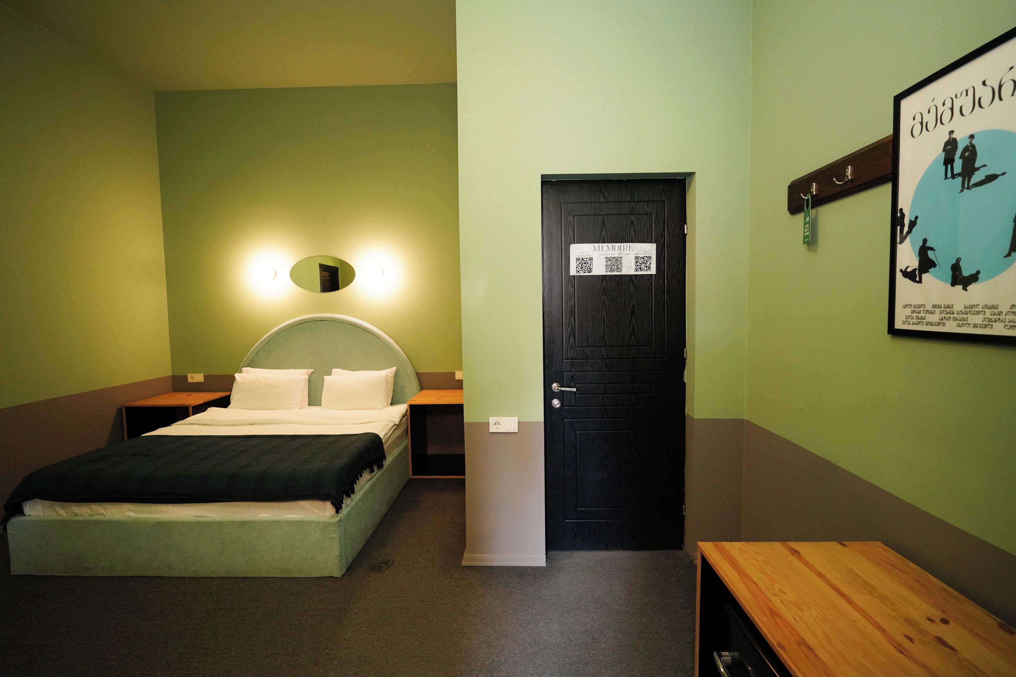 Quarto de hotel com cama, mesa de cabeceira e porta com placa.