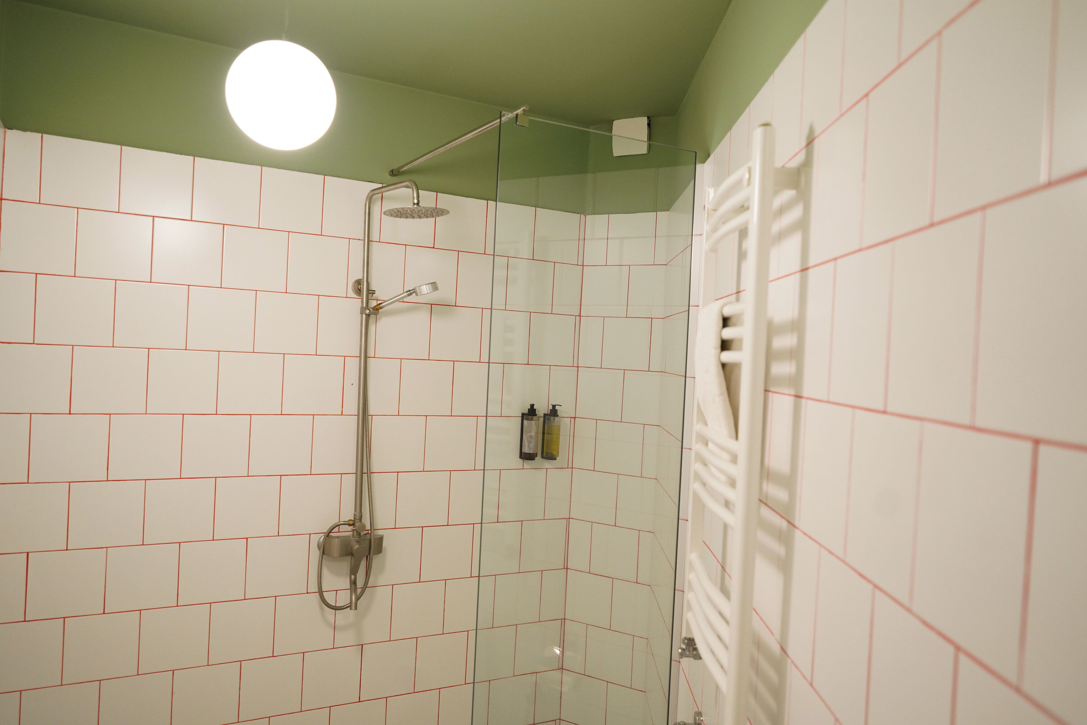 Ducha con puerta de vidrio, paredes de azulejos blancos y techo verde.