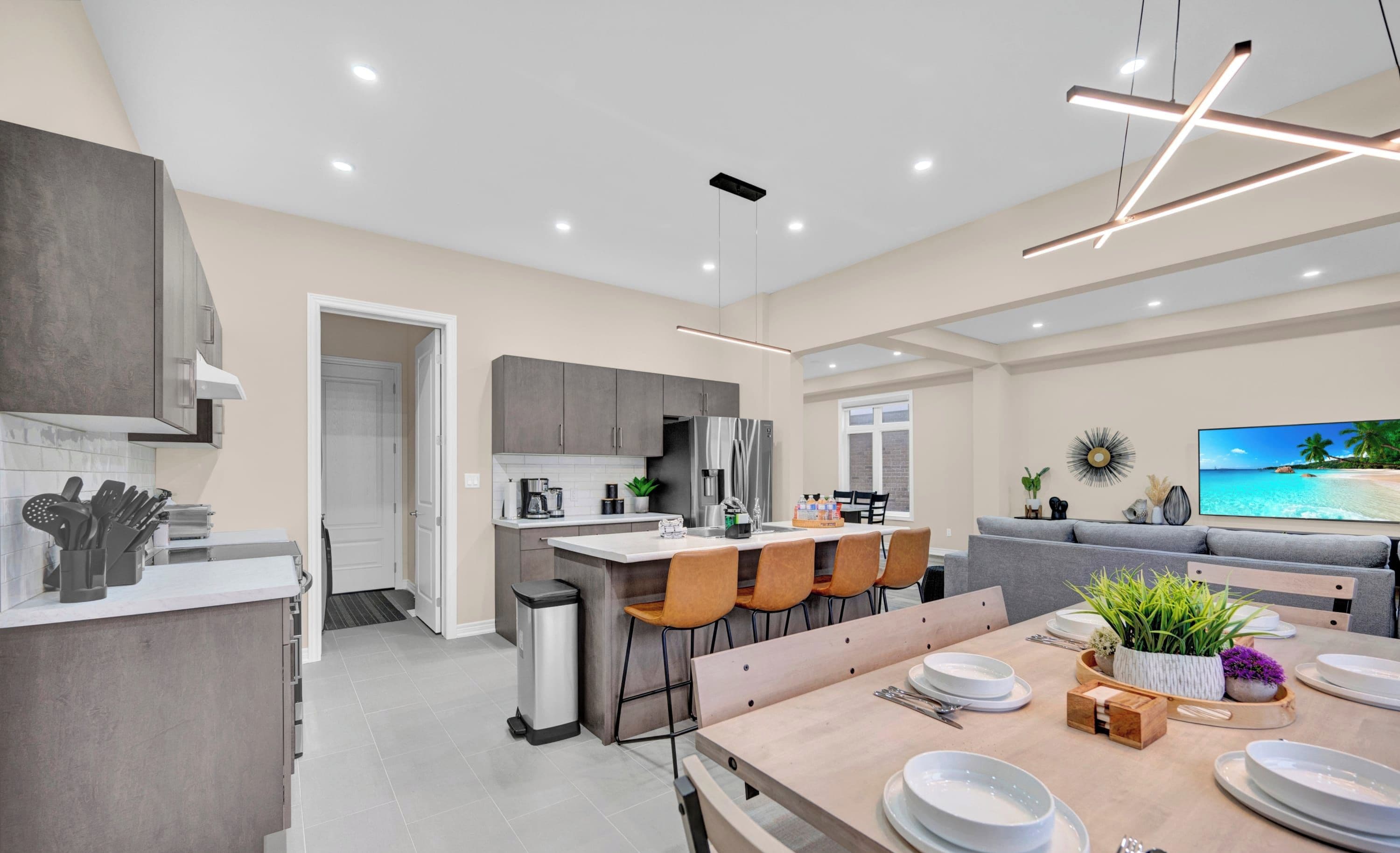 A modern kitchen with grey cabinets, a dining area with a wooden table set for four, and a grey sofa in the living area.