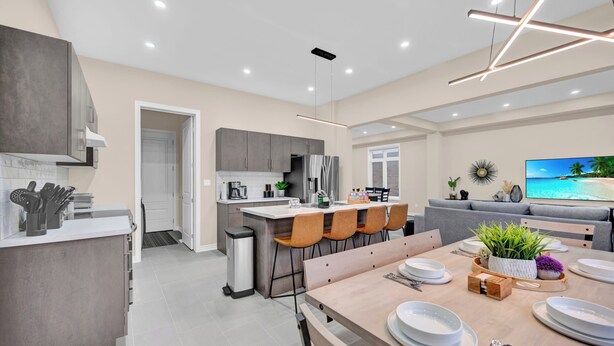 Une cuisine moderne avec des meubles gris, un coin repas avec une table en bois dressée pour quatre personnes, et un canapé gris dans le salon.