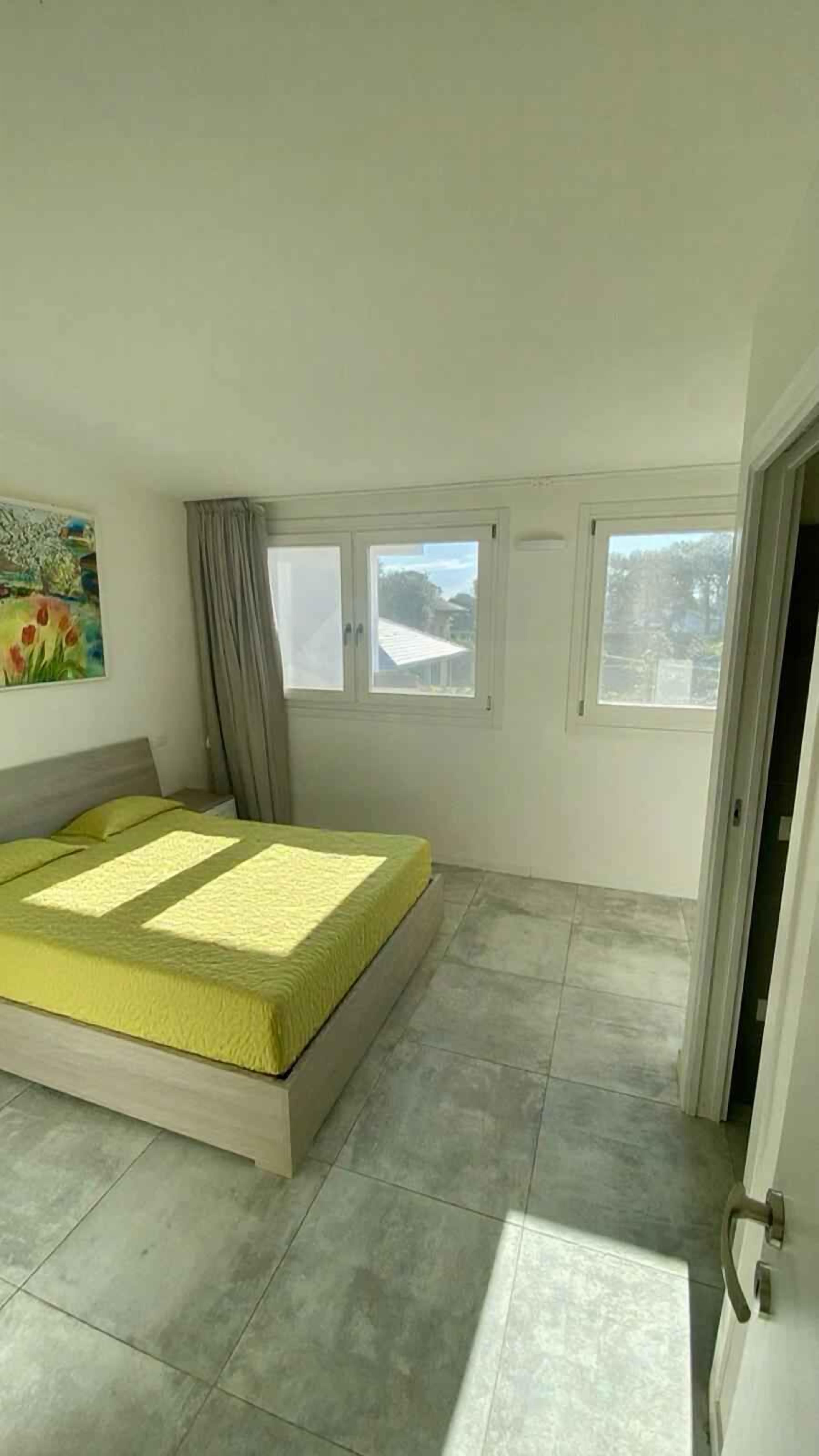 Un dormitorio con una cama, dos ventanas, un cuadro y una puerta.