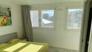 A bedroom with a bed, two windows, a painting, and a door.