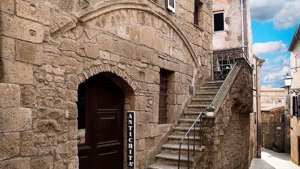 Un bâtiment en pierre avec une porte en bois sombre, un escalier et une enseigne sur laquelle on peut lire « ANTICHITA ».