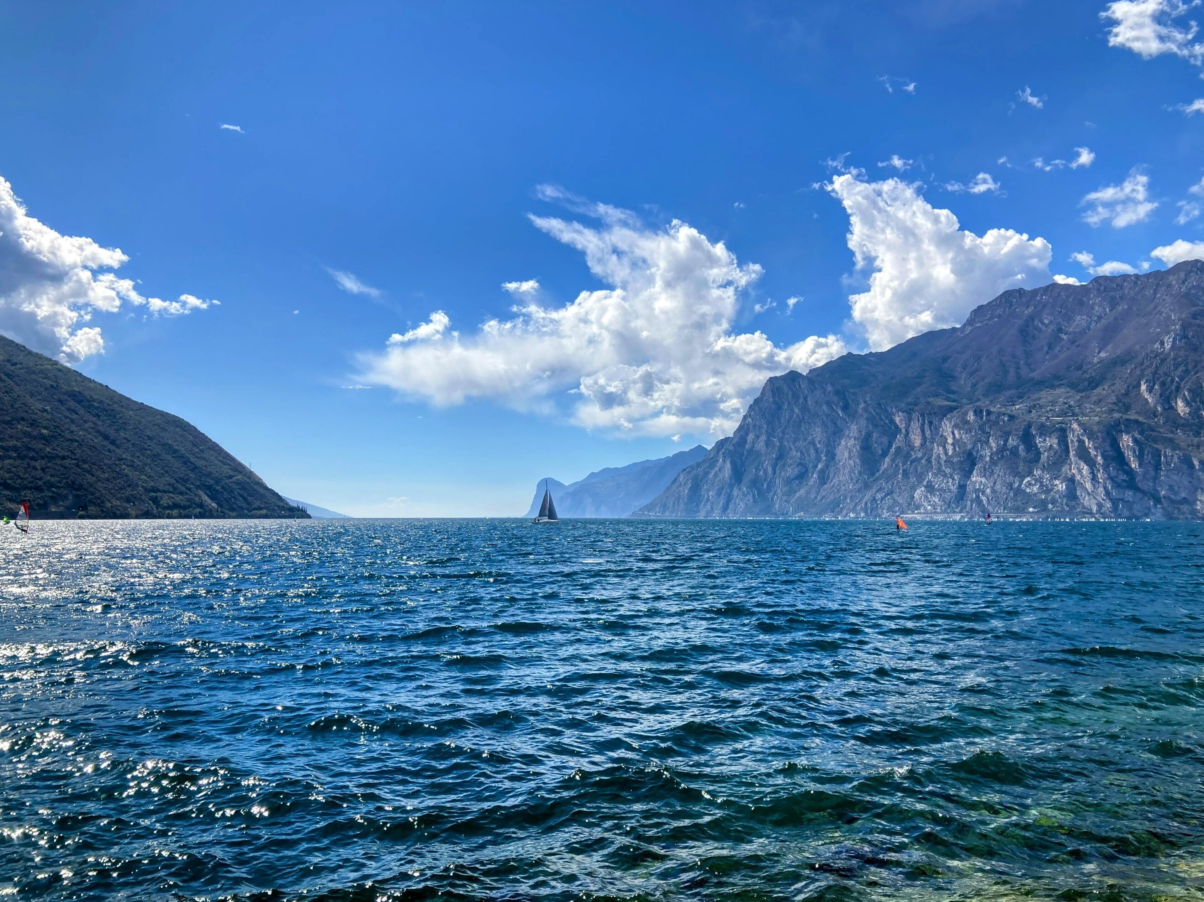 A clear view of a coastal area with a sailboat on the water, surrounded by mountains and a clear sky.