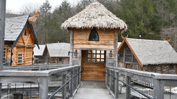A wooden cabin with a thatched roof, accessible via a wooden walkway with railings. - Vikings Villages Resort (Guilford)