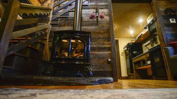 A wooden staircase leading to a room with a wood-burning stove, a wooden wall, and a small shelf with items.