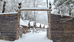 A wooden log cabin with a snow-covered entrance and a wooden fence in a snowy forest. - Vikings Villages Resort (Guilford)
